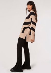 Jersey a rayas beige y negro con corte holgado, mangas largas, aberturas laterales, combinado con pantalones de campana negros acanalados y zapatos negros gruesos.