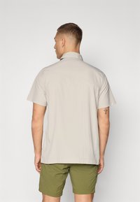 Korte mouwen, lichtbeige shirt van zacht materiaal, met een normale kraag en een rechte zoom, gecombineerd met olijfgroene shorts.