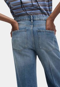 Jasnoniebieskie jeansy denimowe z wysokim stanem, posiadające dwie tylne kieszenie i prosty krój nogawek. Materiał ma miękką, wyblakłą teksturę.