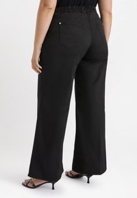 Black wide-leg pants with an elastic waist, back pockets, and a smooth texture, paired with strappy black heels.