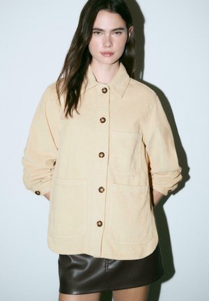 Corduroy jas in lichtbeige, met een kraag, bronzen knopen en twee voorzakken. Gladde textuur, relaxte pasvorm.