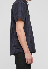 Camicia a maniche corte a quadri in blu scuro e nero, con colletto abbottonato, taschino singolo sul petto e una vestibilità rilassata.