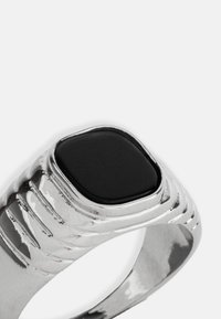 Sidabrinis žiedas su kvadratiniu juodu akmeniu, su tekstūruotais juostomis ir poliruotu paviršiumi, demonstruojantis modernų geometrinį dizainą.