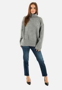 Pull à col roulé gris surdimensionné avec une finition texturée, associé à un jean en denim bleu et des escarpins noirs à bout pointu.