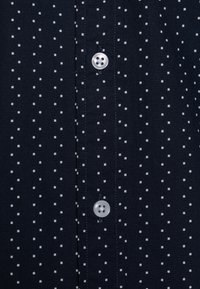 Marineblauwe stof met kleine witte vierkante stippen, met in het midden twee verticaal genaaide witte knopen.