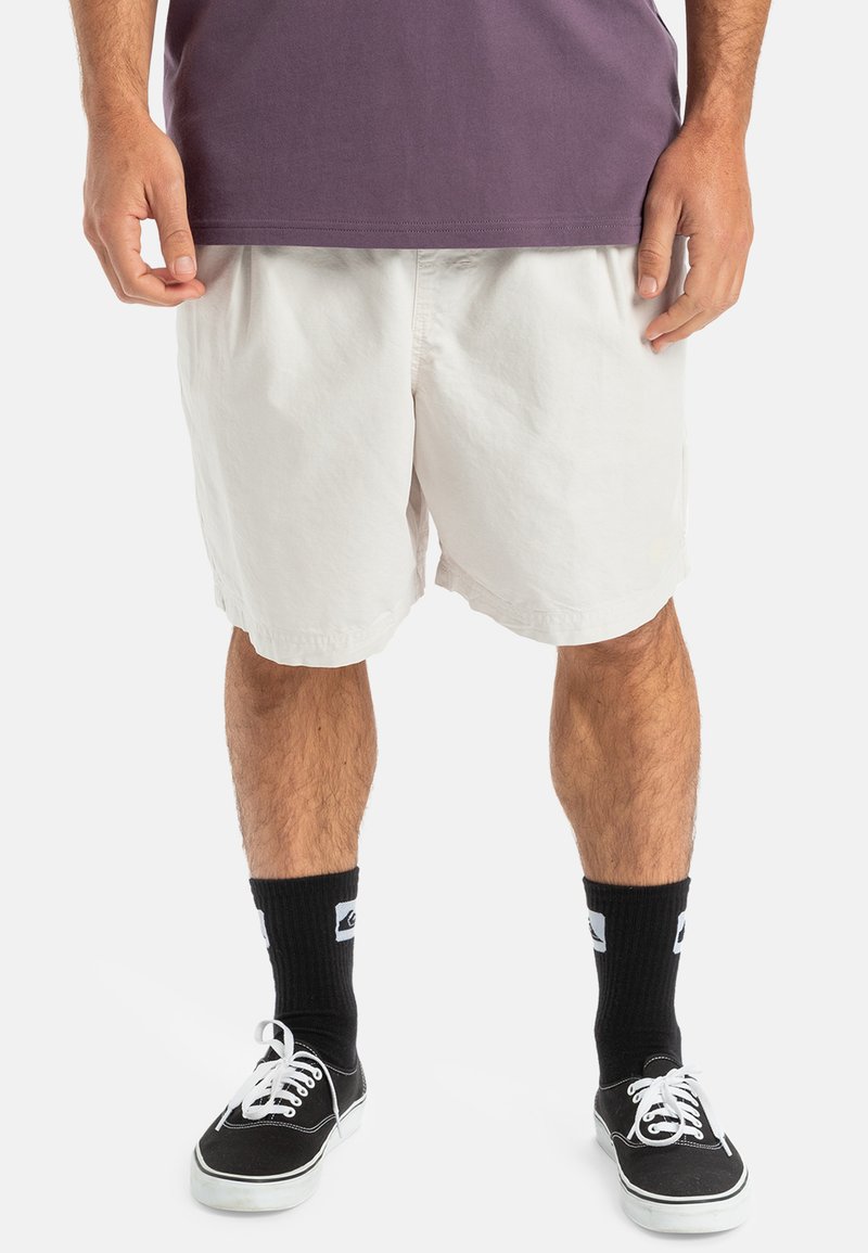 Shorts en coton blanc avec une taille élastique, stylés avec une coupe ample. Associés à des chaussettes de sport noires et des baskets en toile noires.