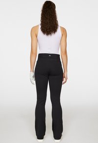 Svarta utsvängda byxor med en slät textur, hög midja med en logotyp och en figurnära design, kombinerade med en ljus linne och handskar.