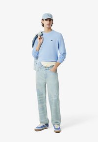 Lichtblauwe sweatshirt, lichtblauwe pet, oversized vervaagde spijkerbroek en blauwe sneakers met tan zolen. Casual outfit met minimale branding.