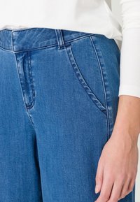 Jean en denim bleu à la texture lisse, avec une taille mi-haute, des poches latérales et un léger délavage le long des jambes. Design simple.