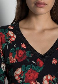 Blommig stickad tröja med svart bakgrund, med röda och elfenbensvita rosor. V-ringning med en strukturerad, svart glittrig kant.