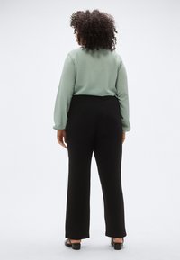 Τοπ μακρυμάνικο σε μέντα πράσινο, συνδυασμένο με μαύρο παντελόνι φάρδιου ποδιού. Το τοπ έχει απαλό ύφασμα, ενώ το παντελόνι διαθέτει ελαστική μέση.