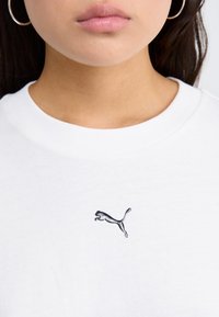Hvit bomull t-skjorte med rund hals og en svart brodert Puma-logo av en sprettende katt plassert på brystområdet.
