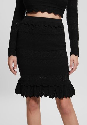 Personne portant un crop top noir à manches longues et une jupe assortie longueur genou avec texture dentelle et ourlets festonnés, debout.