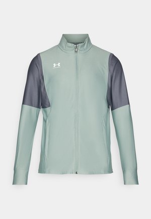 Világoszöld zipzáras dzseki sötétszürke ujjakra, sima textúrával és oldalsó zsebekkel. Az elülső részen az Under Armour logó található.