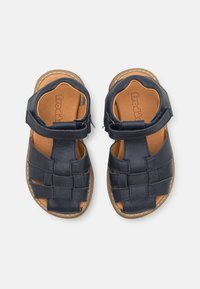 Mørkeblå læråpne sandaler med vevd stroppedesign og justerbar ankelrem, med en tan polstret fotseng og sydd såle.