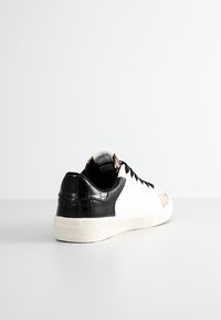 Sneaker bianca con tallone in pelle di coccodrillo nera, accento laterale in morbido marrone chiaro e lacci neri; suola in gomma con grip testurizzato.