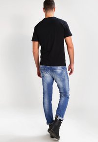 Schwarzes T-Shirt mit kurzen Ärmeln, kombiniert mit hellblauen Jeans aus Denim. Die Jeans weisen einen leichten Farbverlauf auf und haben ein klassisches Fünf-Taschen-Design, getragen mit schwarzen Stiefeln.