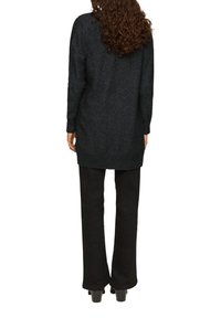 Schwarzer, langärmliger Pullover mit lockerer Passform, strukturiertem Stoff und geripptem Saum, kombiniert mit schwarzen Glockenhosen und Plateauschuhen.