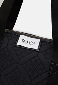 Schwarze, gesteppte Tragetasche mit geometrischem Muster, schwarzem Zubehör und einem auffälligen weißen Etikett mit dem Text "DAY ET BIRGER ET MIKKELSEN".