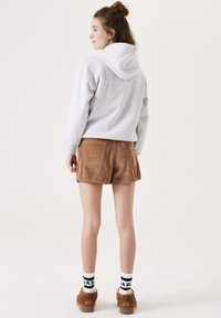 Grijze hoodie met een relaxte pasvorm, gecombineerd met bruine corduroy shorts. Witte sokken met zwarte graphics en bruine schoenen maken de outfit compleet.