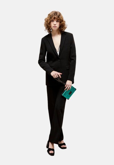 Completo nero su misura con blazer a un solo bottone, pantaloni a gamba larga, abbinati a una borsa teal e sandali neri. Tessuto liscio, taglio moderno.