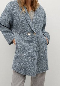 Cappotto doppiopetto in tessuto herringbone blu testurizzato con due grandi bottoni, ampi rever e tasche laterali, caratterizzato da una vestibilità comoda.
