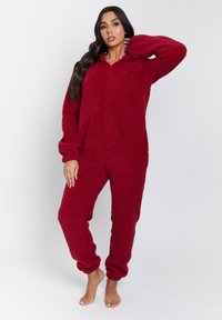 Un mono rojo y esponjoso hecho de tela suave con textura; cuenta con capucha, mangas largas y puños elásticos en ankles y muñecas.
