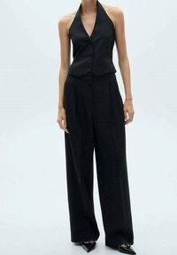 Sort halternecktop med knappedetaljer kombineret med højttaljede, vidde bukser. Snyde sorte stiletter med spids tå fuldender looket.