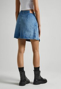 Gonna di jeans blu chiaro con orlo sfrangiato, vita aderente e dettagli in pelle sulla parte posteriore, abbinata a stivali militari neri e calzettoni a coste.