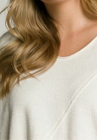 Top bianco con texture e design a V. Il tessuto appare morbido e leggermente rigato, con una vestibilità rilassata e dettagli di cucitura sottili.