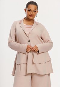 Roze gelaagde blazer met een reverskraag, enkele knoopsluiting en lange mouwen, gecombineerd met een satijnen top die de textuur versterkt.