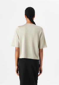 Short-sleeve, light gray top with a relaxed fit. Soft, smooth fabric, minimal stitching details, worn over a black, form-fitting skirt.
