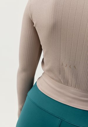 Lange mouw ribbeltrui in lichtbeige met een getailleerd ontwerp, voorzien van een subtiele logodetail. Gepaard met hooggesneden teal leggings.