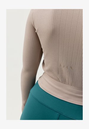 Lange mouw ribbeltrui in lichtbeige met een getailleerd ontwerp, voorzien van een subtiele logodetail. Gepaard met hooggesneden teal leggings.