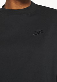 Svart Nike sweatshirt med ribbad textur, rundad halsdesign och en diskret svart broderad logotyp på bröstet.