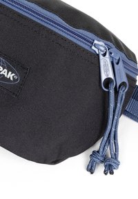 Černý látkový sáček s modrým zipem, s texturovaným povrchem, dvojitými tahátky na zip a vyraženým logem po straně.