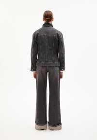 Donkergrijze denimjack met zichtbare stiksels, gecombineerd met bijpassende wijde broek met omgeslagen cuffs. Eenvoudig, klassiek ontwerp.