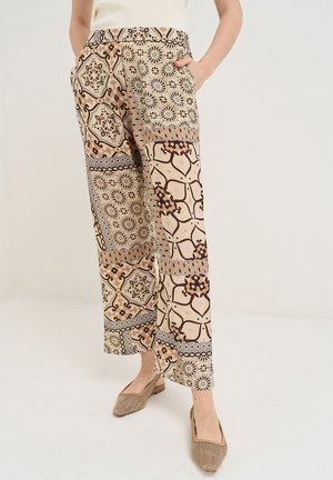 Mujer con pantalones de pierna ancha con patrón patchwork mixto floral y geométrico en tonos beige y marrones, combinados con zapatos planos tejidos beige.