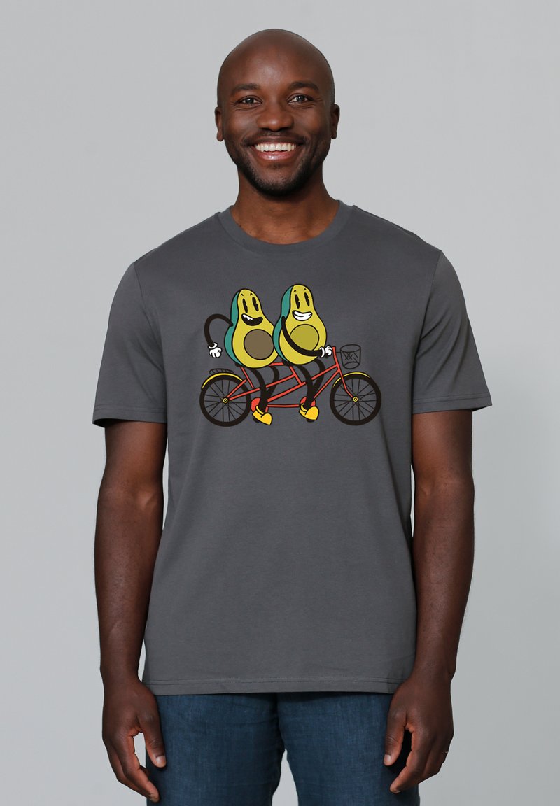 Grijze t-shirt met een cartoonontwerp van twee avocado's die op een rode tandemfiets rijden, met gele accenten en zwarte omlijningen.