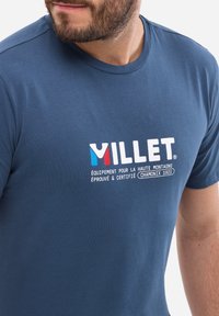 Granatowa koszulka z okrągłym dekoltem, z białym tekstem i kolorowym logo. Miękka w dotyku, z krótkimi rękawami, luźny fason.