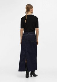 Mørk denim maxi-nederdel med høj slids, baglommer og diskrete syninger, parret med en sort tætsiddende kortærmet top.
