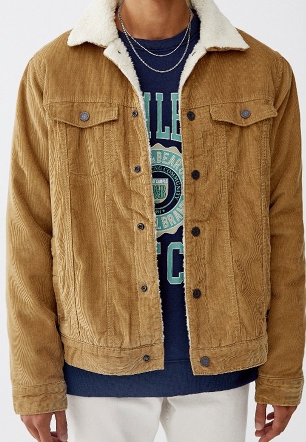 Bruine corduroy jas met een sherpa kraag, voorzakken en zilveren knoopsluitingen. Draag over een marineblauwe graphic sweatshirt, met gelaagde kettingen.