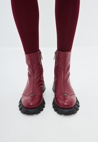 Bottines en cuir bourgogne avec une finition lisse, fermeture éclair et semelle en caoutchouc noir prononcée avec des motifs de traction définis.