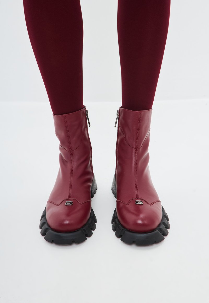 Bottines en cuir bourgogne avec une finition lisse, fermeture éclair et semelle en caoutchouc noir prononcée avec des motifs de traction définis.