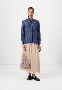 Denimbluse mit Halsband, langen Ärmeln, kombiniert mit einem fließenden beigen Rock. Schwarze Schuhe und eine kleine lila Tasche setzen Akzente zu dem Outfit.