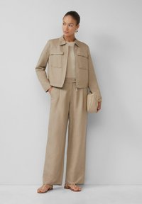 Beige Leinenjacke mit zwei Vorder Taschen, kombiniert mit passenden weiten Hosen und einem strukturierten Oberteil. Akzentuiert mit einer minimalistischen Tasche und Sandalen.