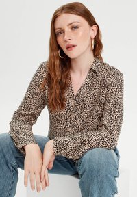 Leopard-Print-Bluse mit Kragen, Knopfverschluss, langen Ärmeln und einem weichen, leichten Material. Getragen mit blauen Jeans.
