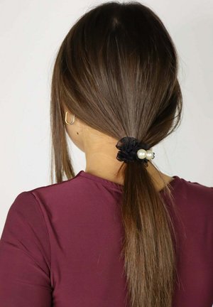 Fascia per capelli nera in tessuto con due grandi perle bianche che tengono i capelli lisci in una coda bassa. Lo sfondo è bianco uniforme e la maglietta è color bordeaux.