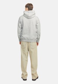 Sudadera gris con capucha y puños y dobladillo de canalé, combinada con pantalones beige claros con detalles de costura en los bolsillos traseros.