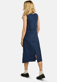Rochie fără mâneci din denim bleumarin, cu corp strâmt și două buzunare în spate. Are o deschizătură până la genunchi pentru libertate de mișcare.